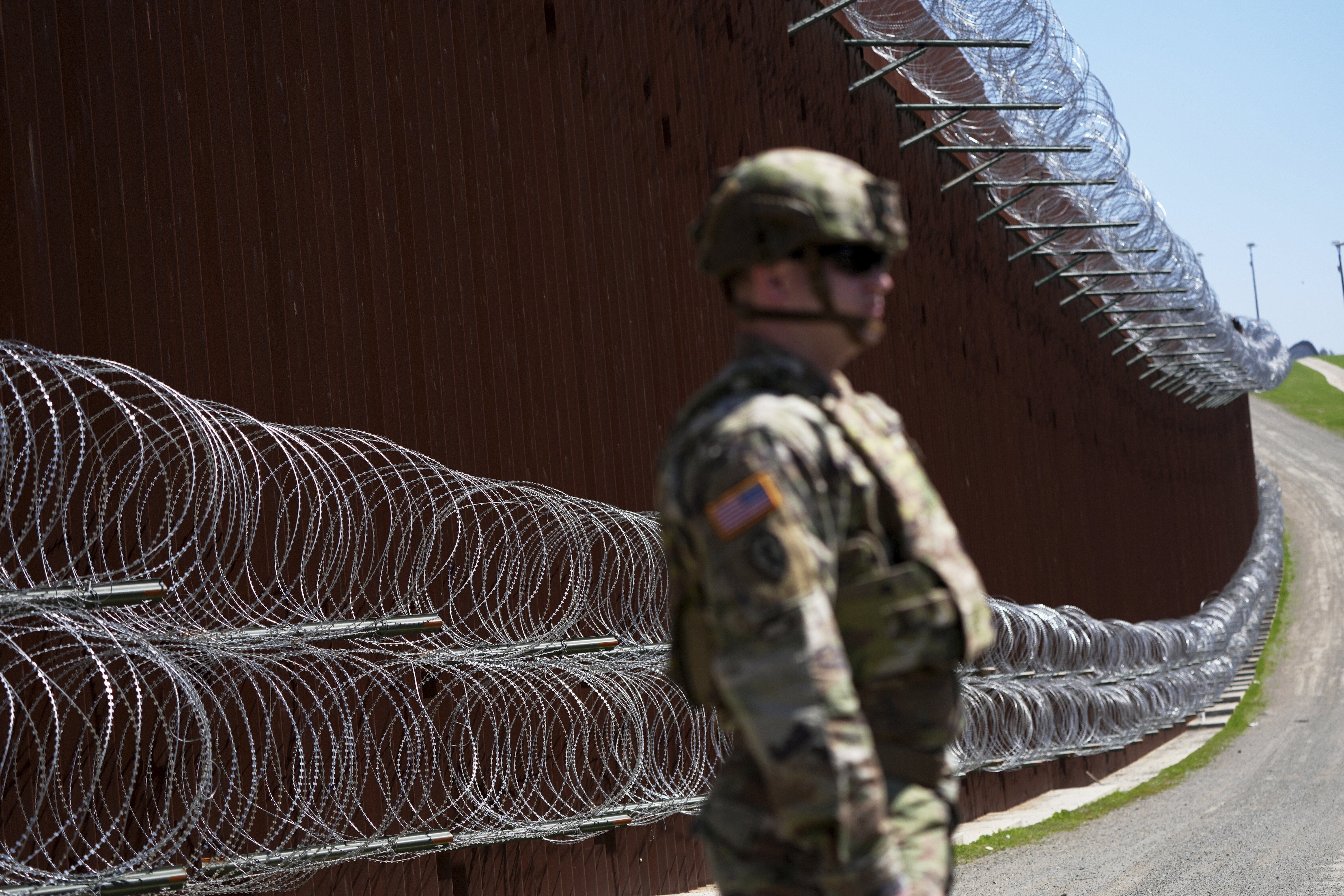 A member of the military looks on in front of newly-installed concertina wire lining one of two border walls separating Mexico from the United States on March 21 in San Diego. (AP Photo/Gregory Bull)