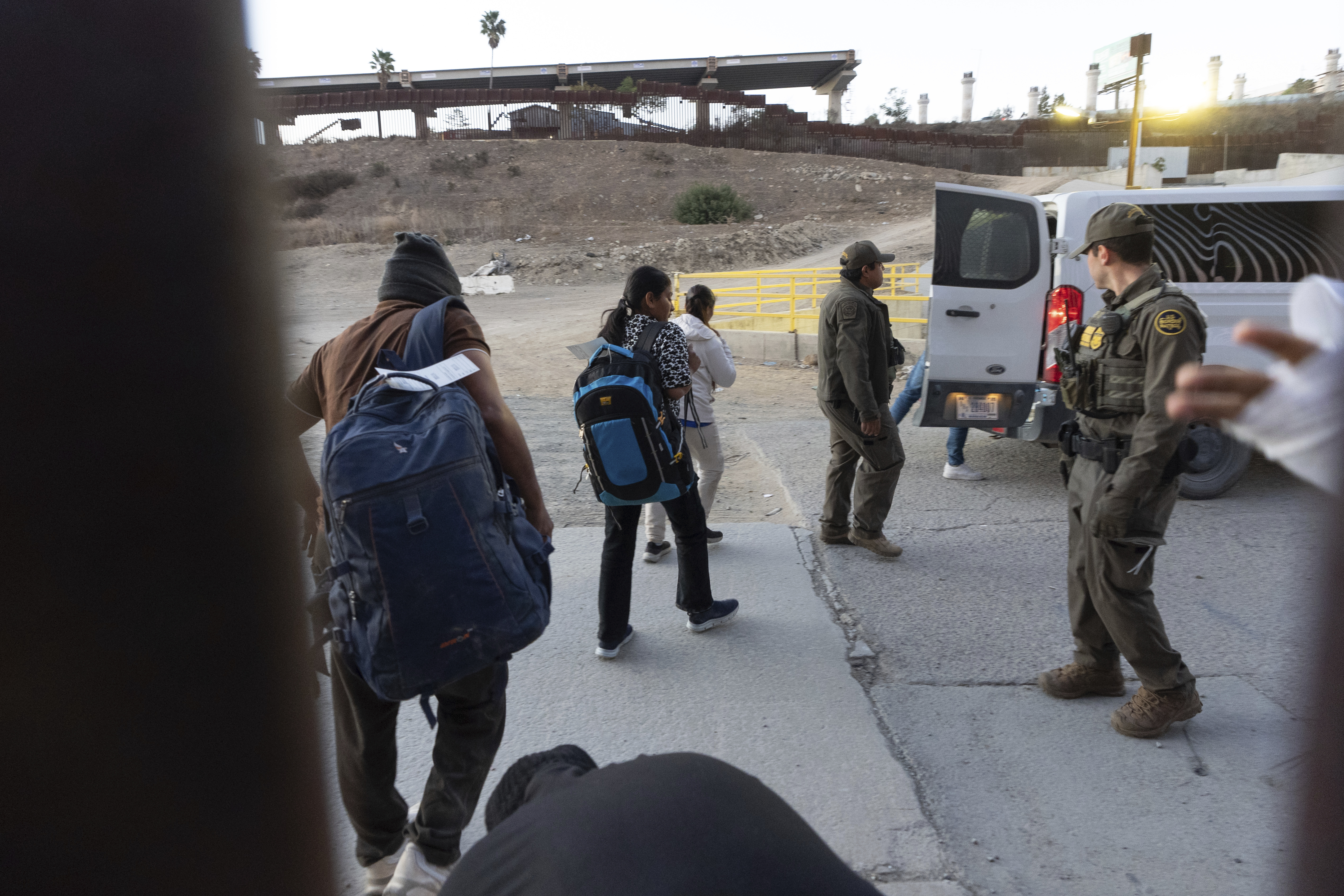 Migrants make their way to a Border Patrol van after crossing illegally and waiting to apply for asylum between two border walls separating Mexico and the United States in January. (AP Photo/Gregory Bull).