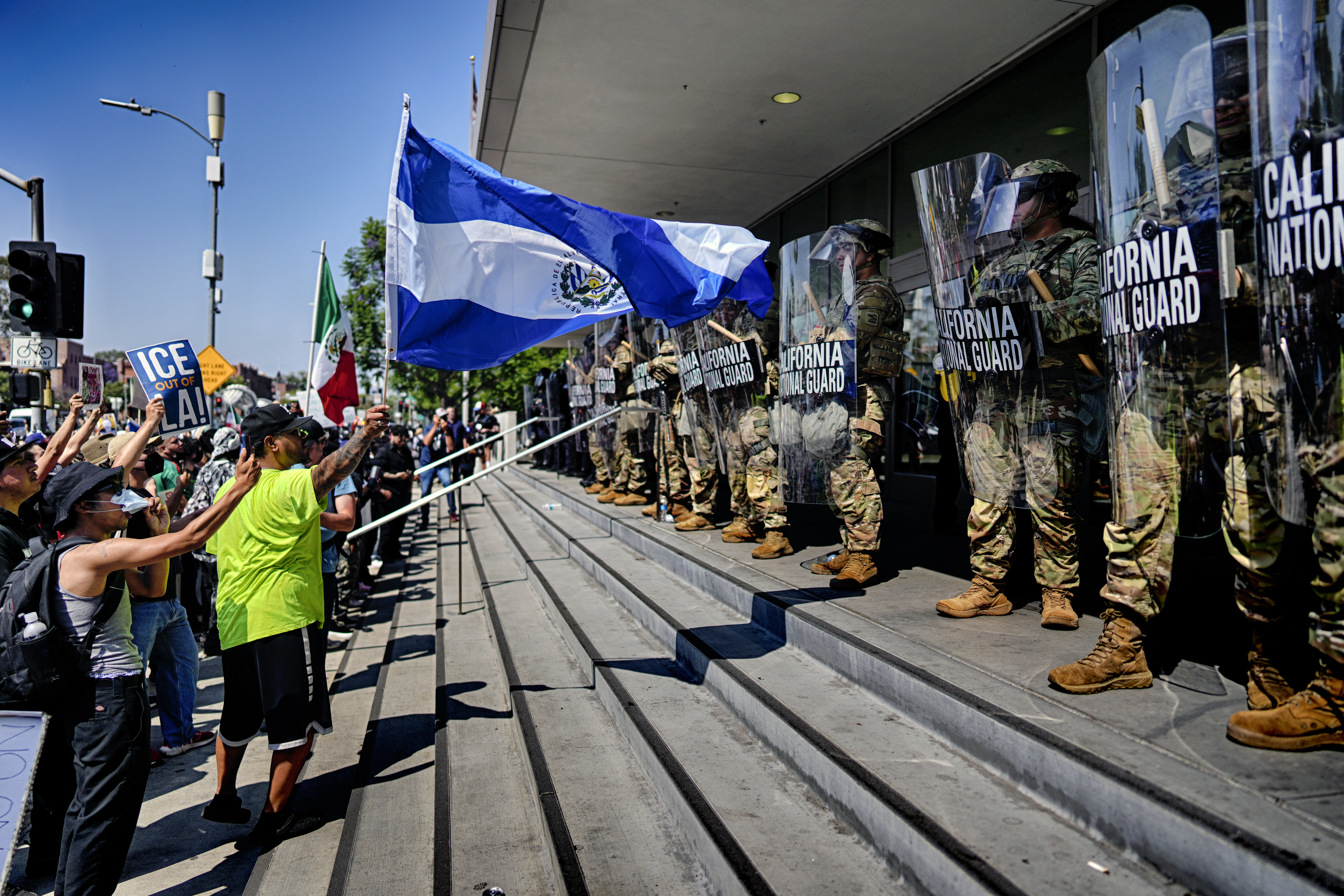 A protester waves a National Flag of El Salvador in front of a line of California National Guard in front of Federal Building on Monday in downtown Los Angeles. (AP Photo/Eric Thayer).