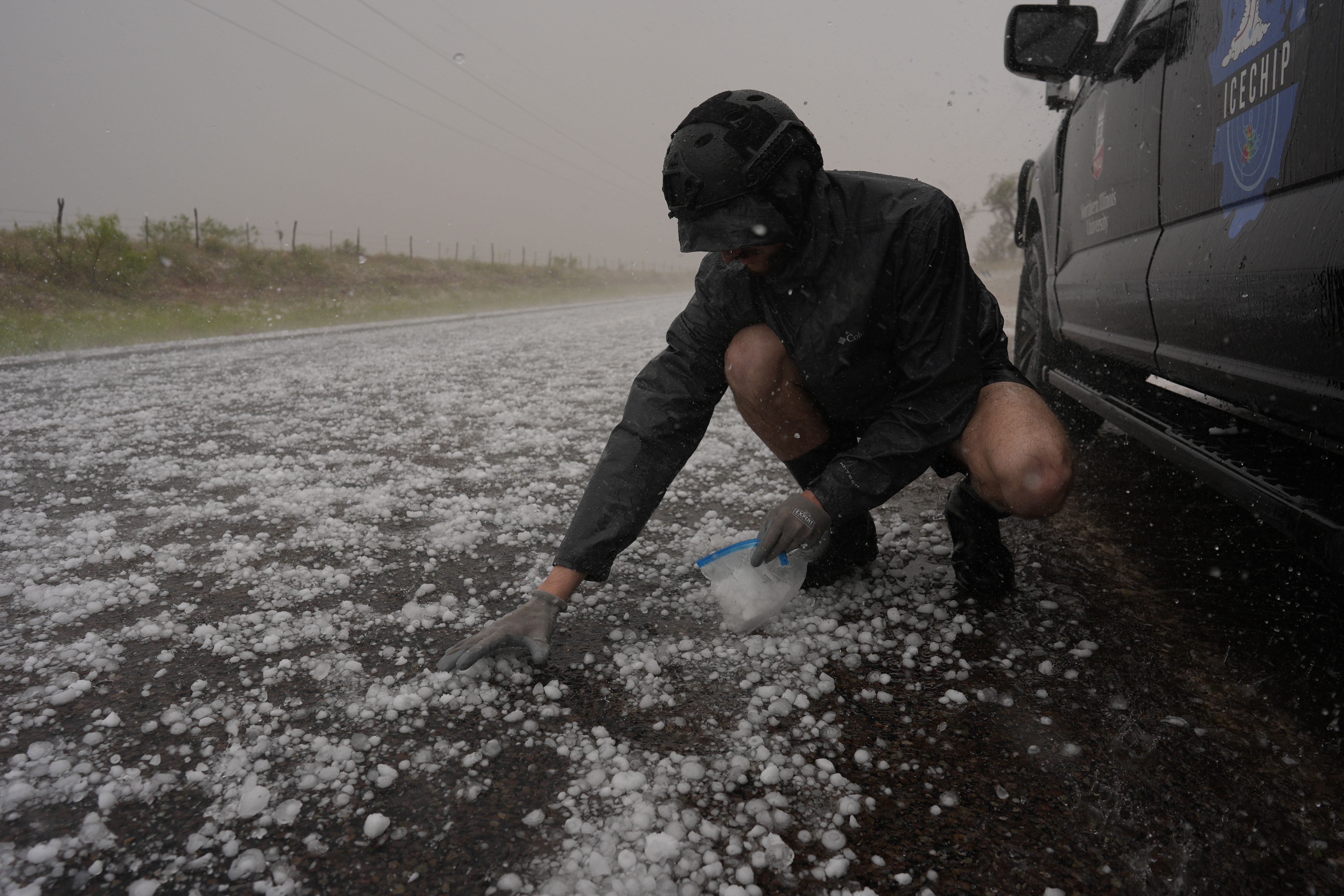 Tony Illenden crouches in a helmet and gloves outside Northern Illinois University's Husky Hail Hunter vehicle to scoop hail into a bag during a storm while on a Project ICECHIP operation on Friday. (AP Photo/Carolyn Kaster).