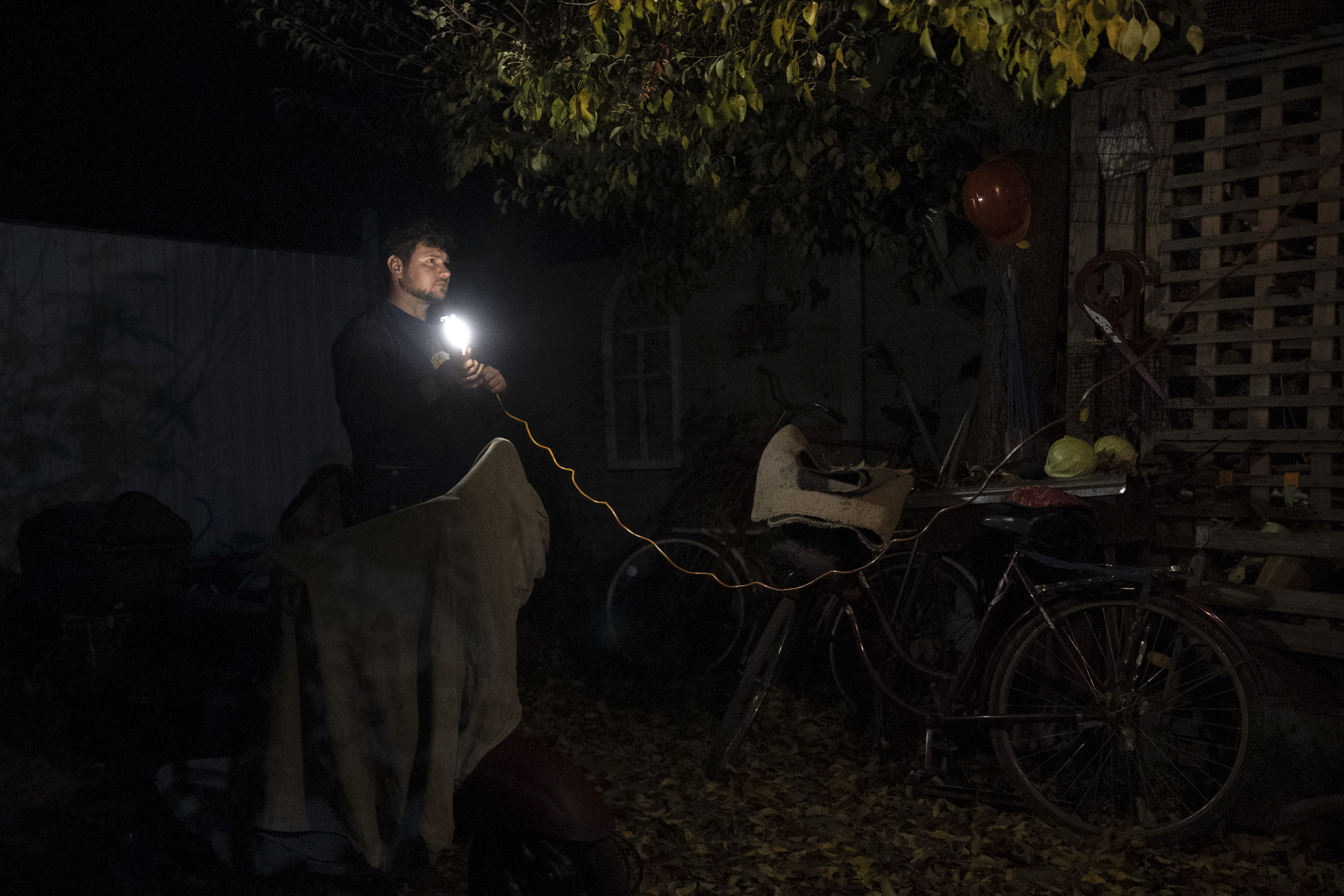 Energy worker Oleksandr Adamchuk rigs up a light in his yard to fix a moped in the Kyiv region.