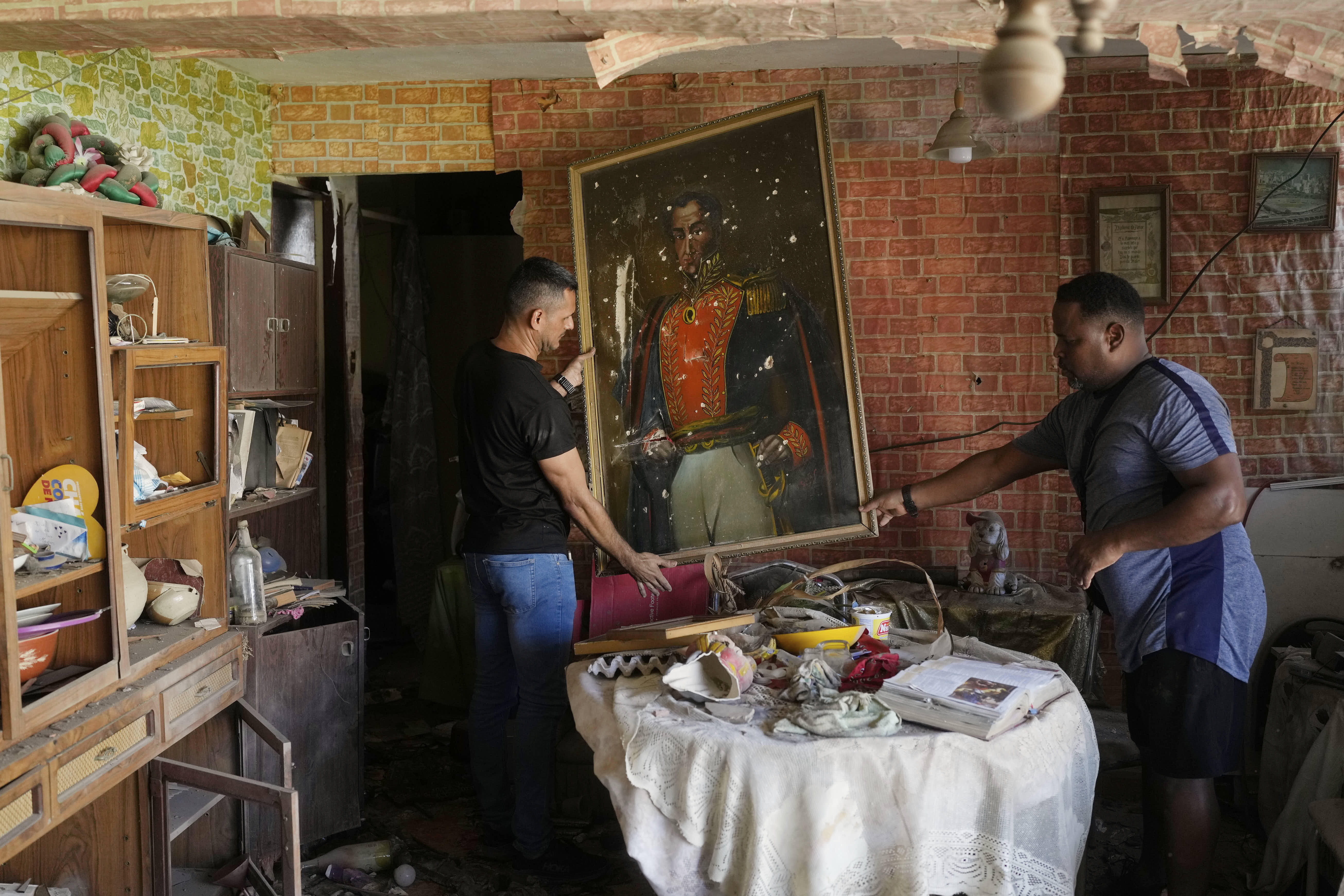 People remove a damaged painting in a home which they say was hit during U.S. military operations to capture the Venezuelan president in Catia La Mar.