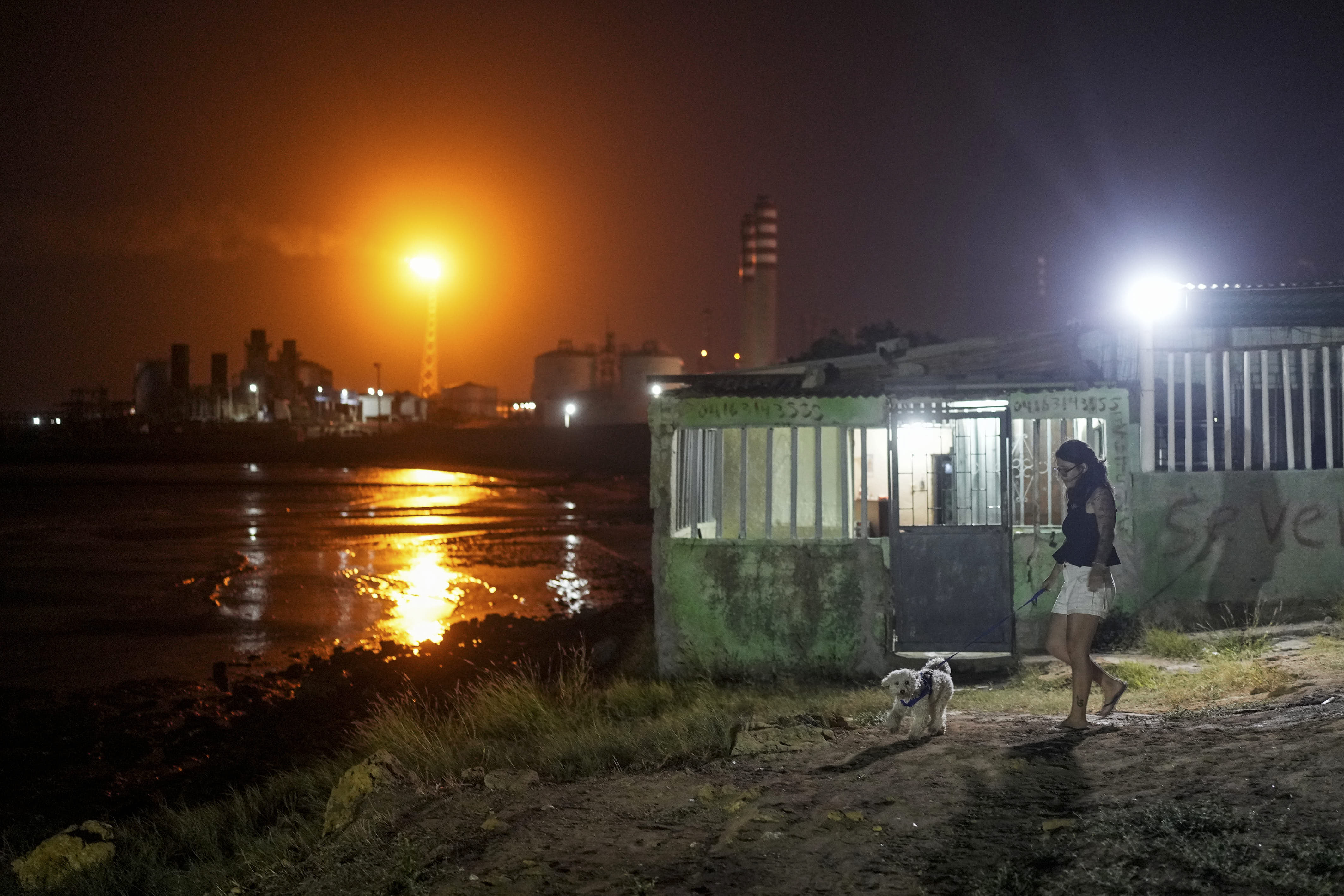A woman walks her dog as flames burn from flare stacks from a Venezuelan oil refinery in Punta Cardon.