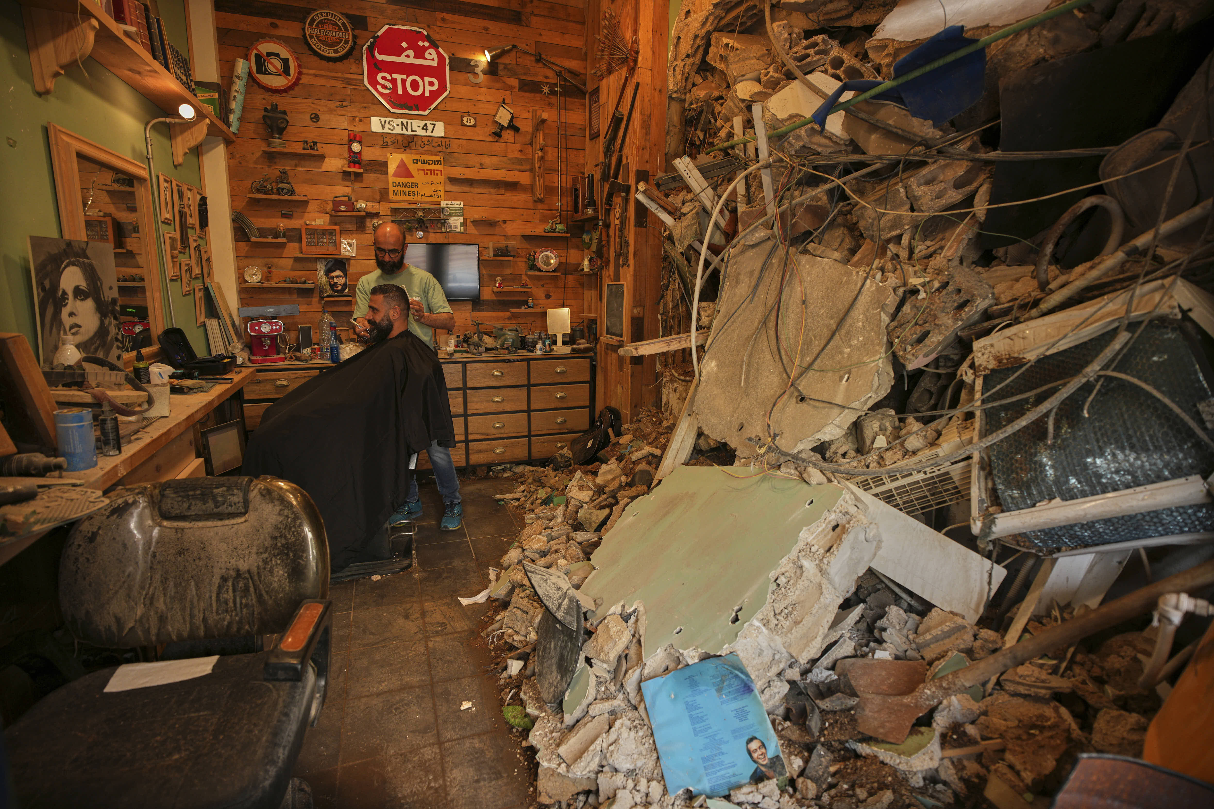 A barber cuts the hair of a client inside his shop damaged in an Israeli airstrike, in Lebanon.