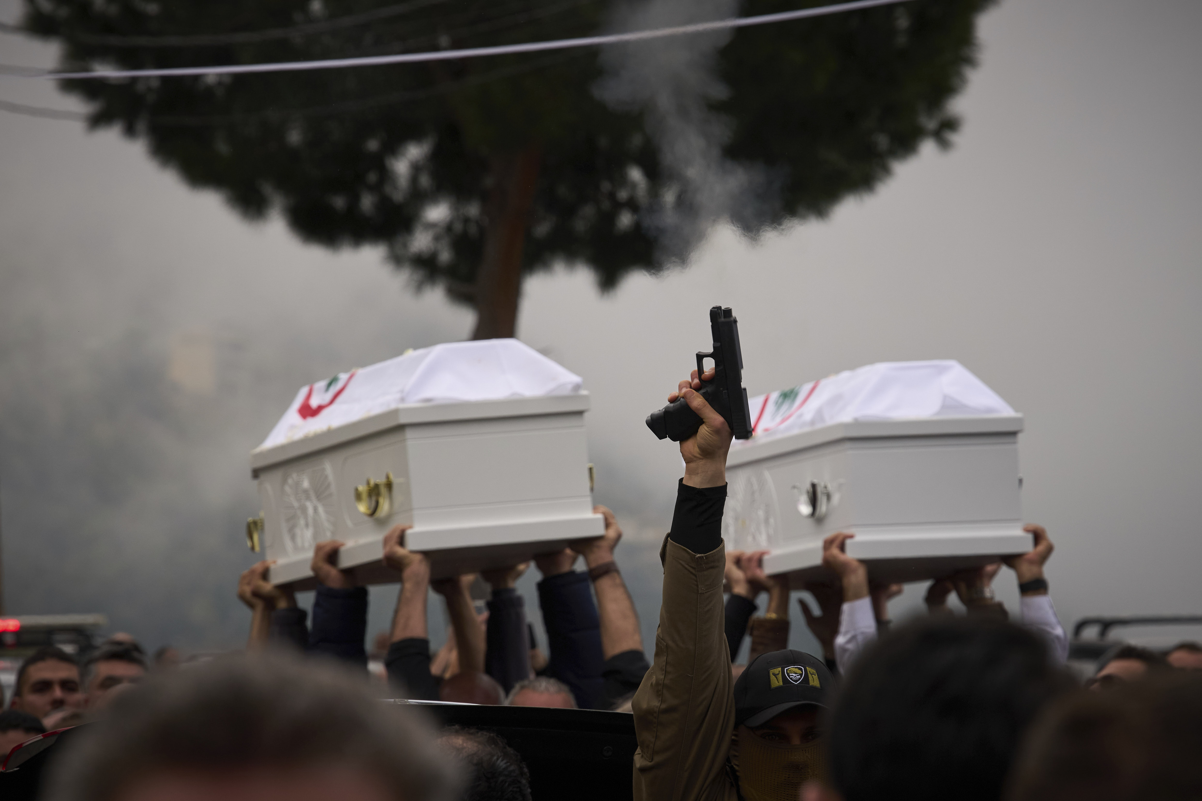 A gunman fires his gun as men carry coffins during a funeral in Yahshush, Lebanon. 