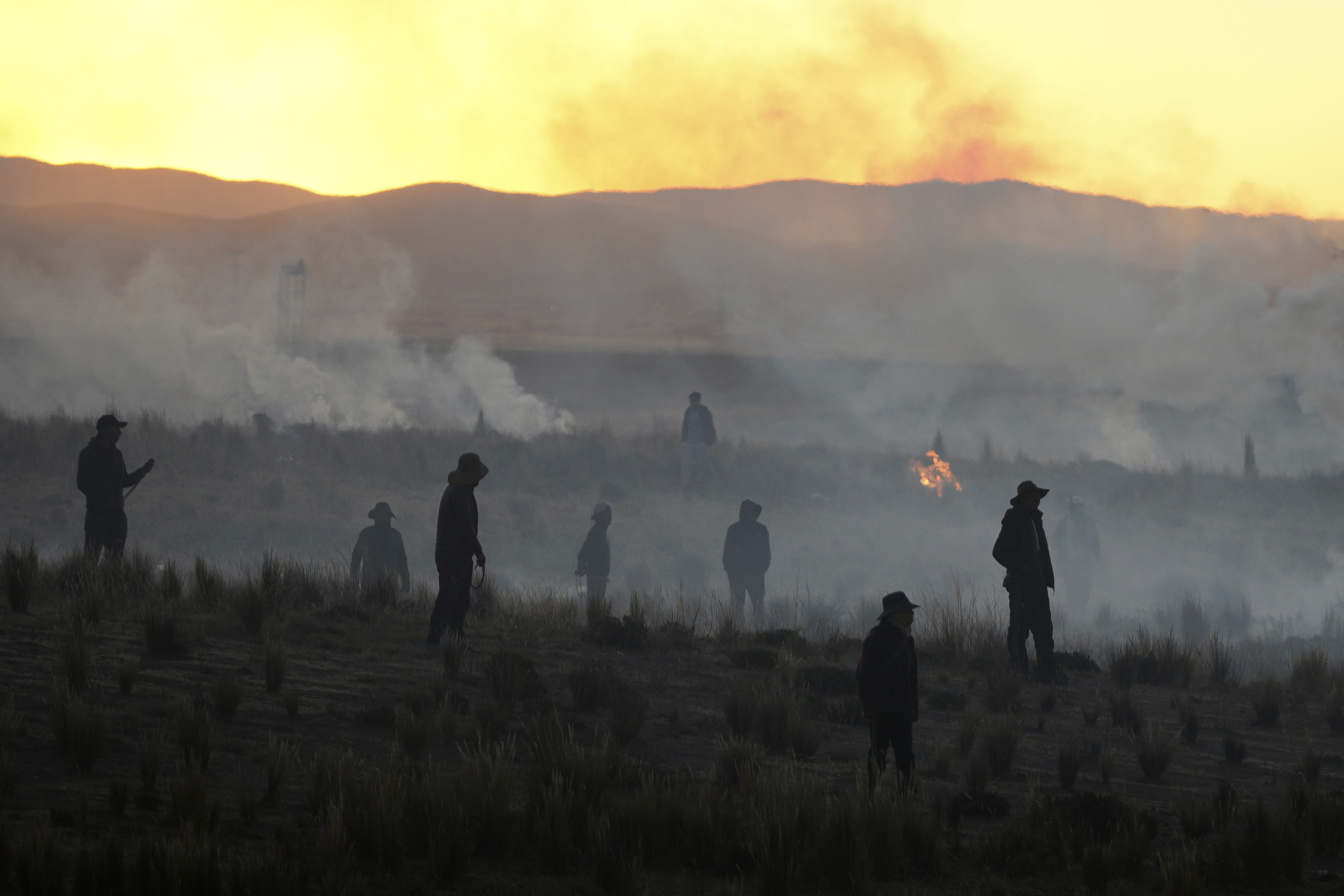 Anti-government protesters standing in a field are silhouetted against clouds of tear gas launched by police, near El Alto. 