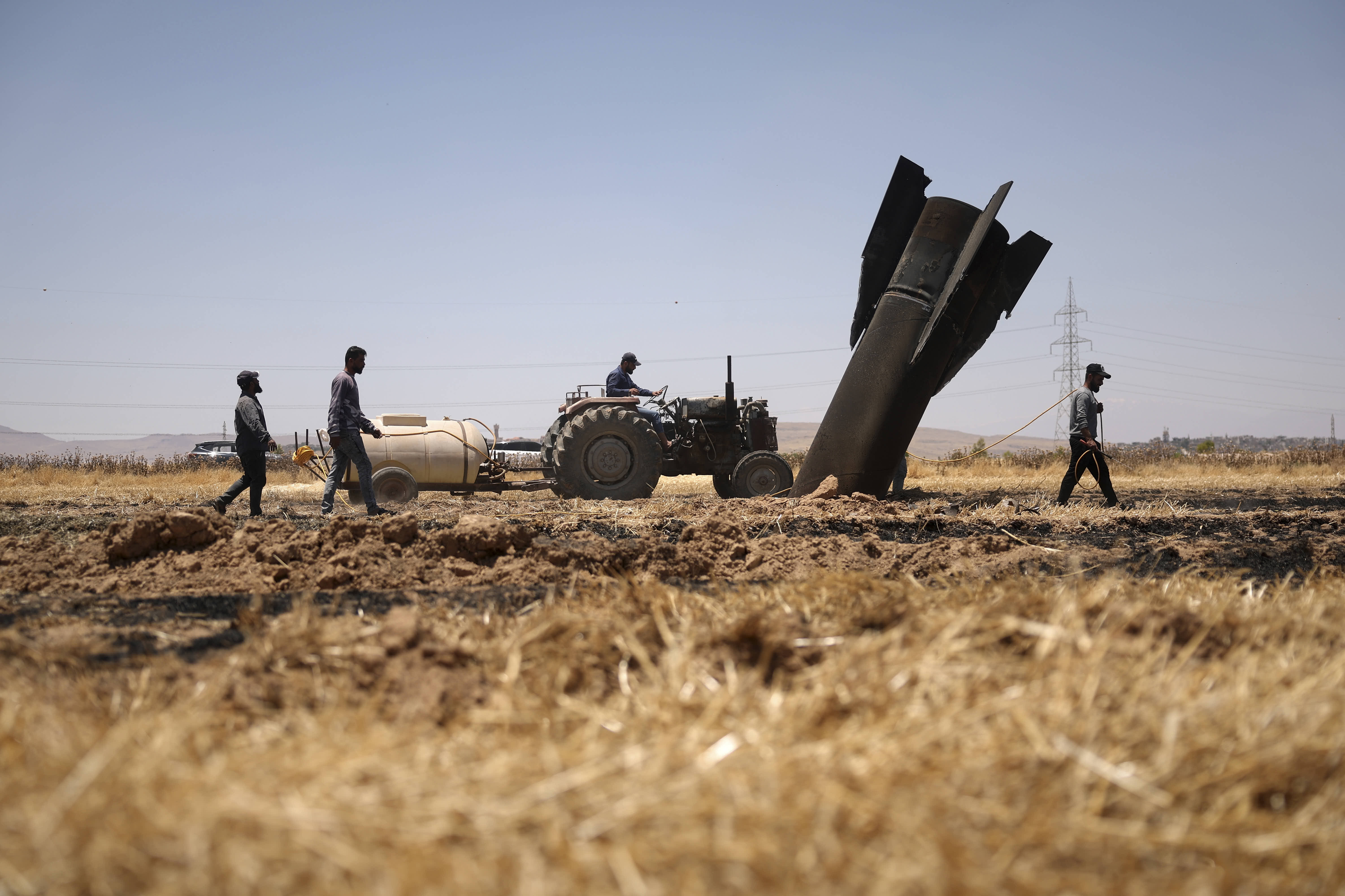 Farmers spray water on a scorched field next to a projectile near Najha.