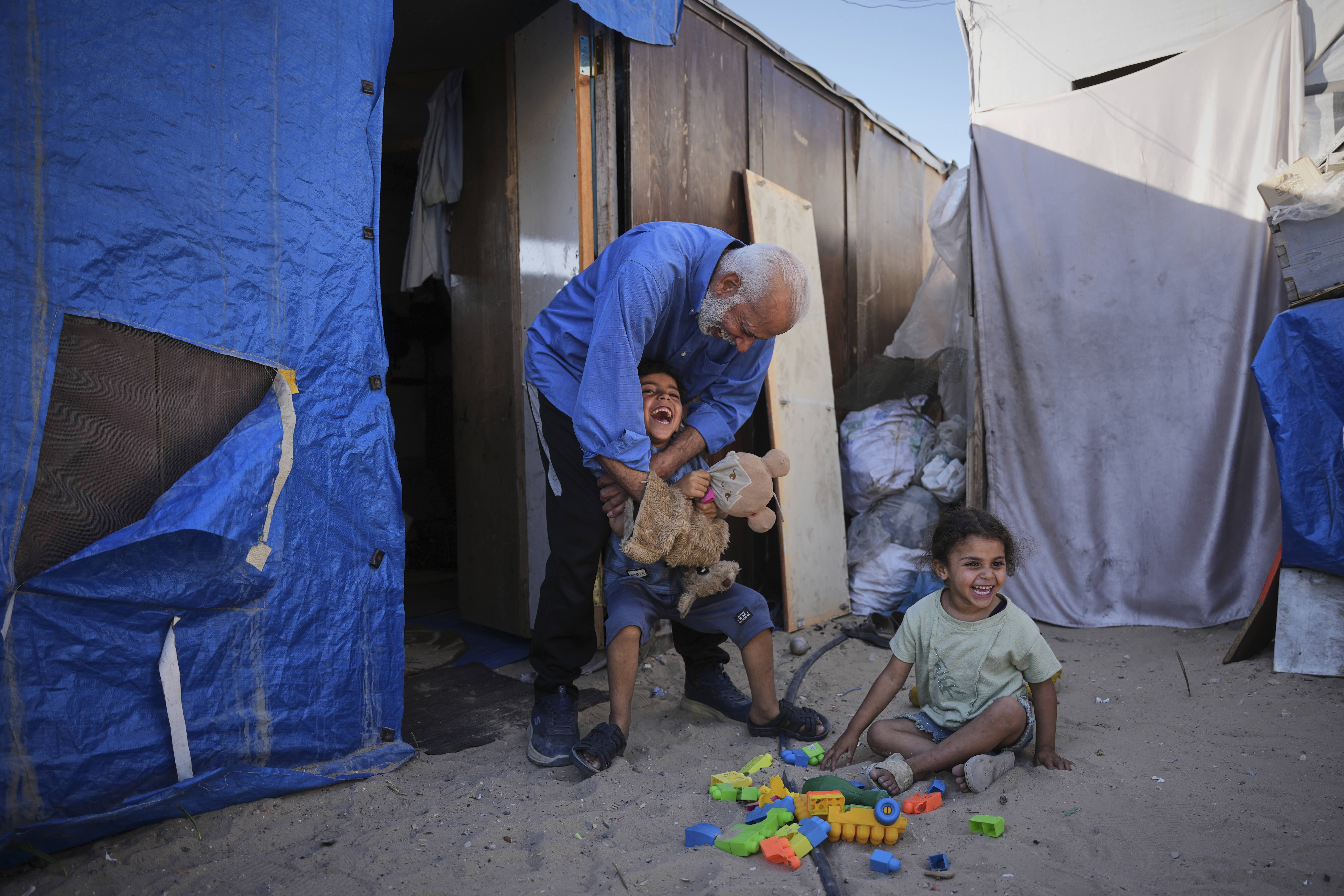 Mahmoud Nofal plays with his grandchildren outside their tent in Khan Younis.
