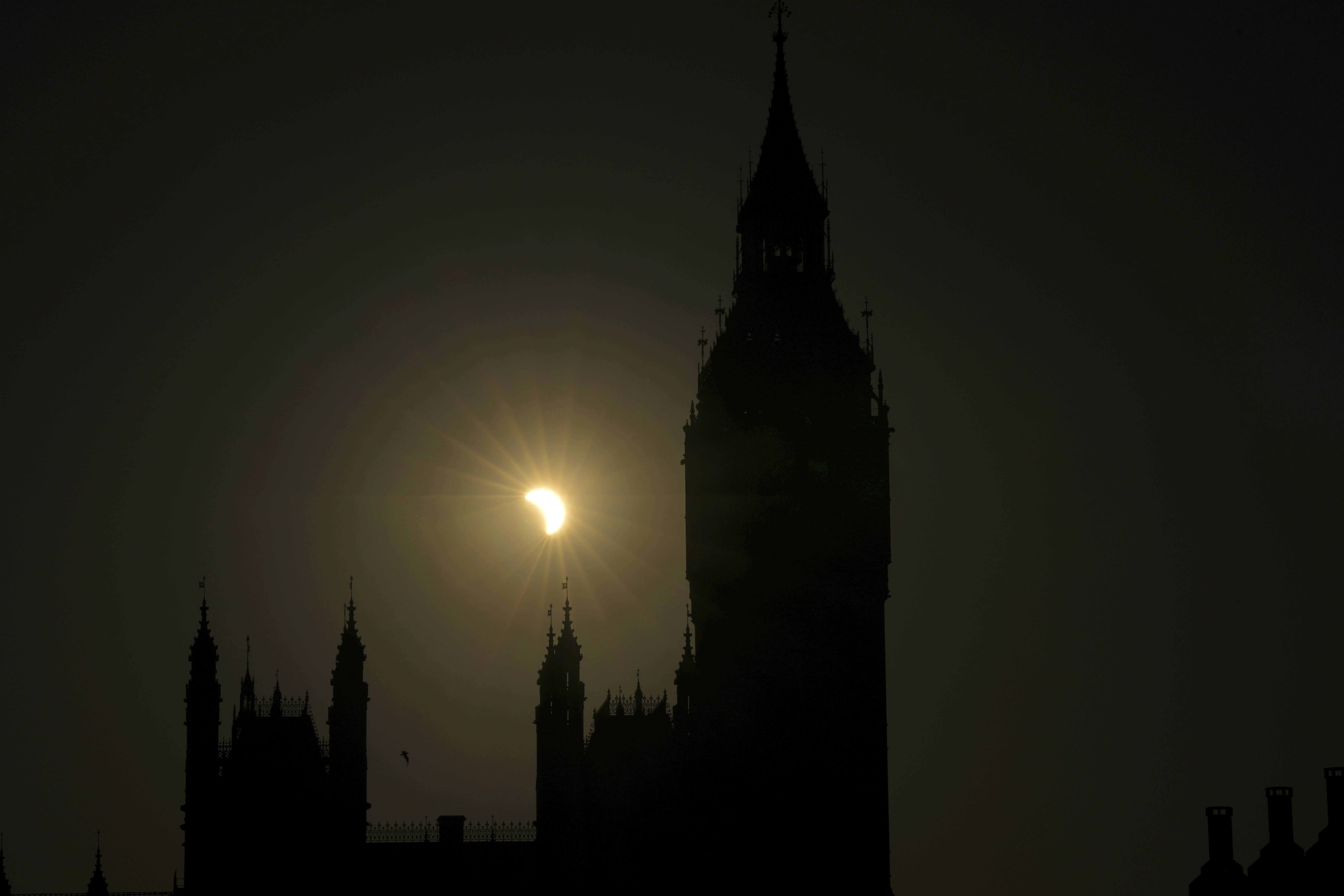 A partial solar eclipse is visible next to the Houses of Parliament in London.