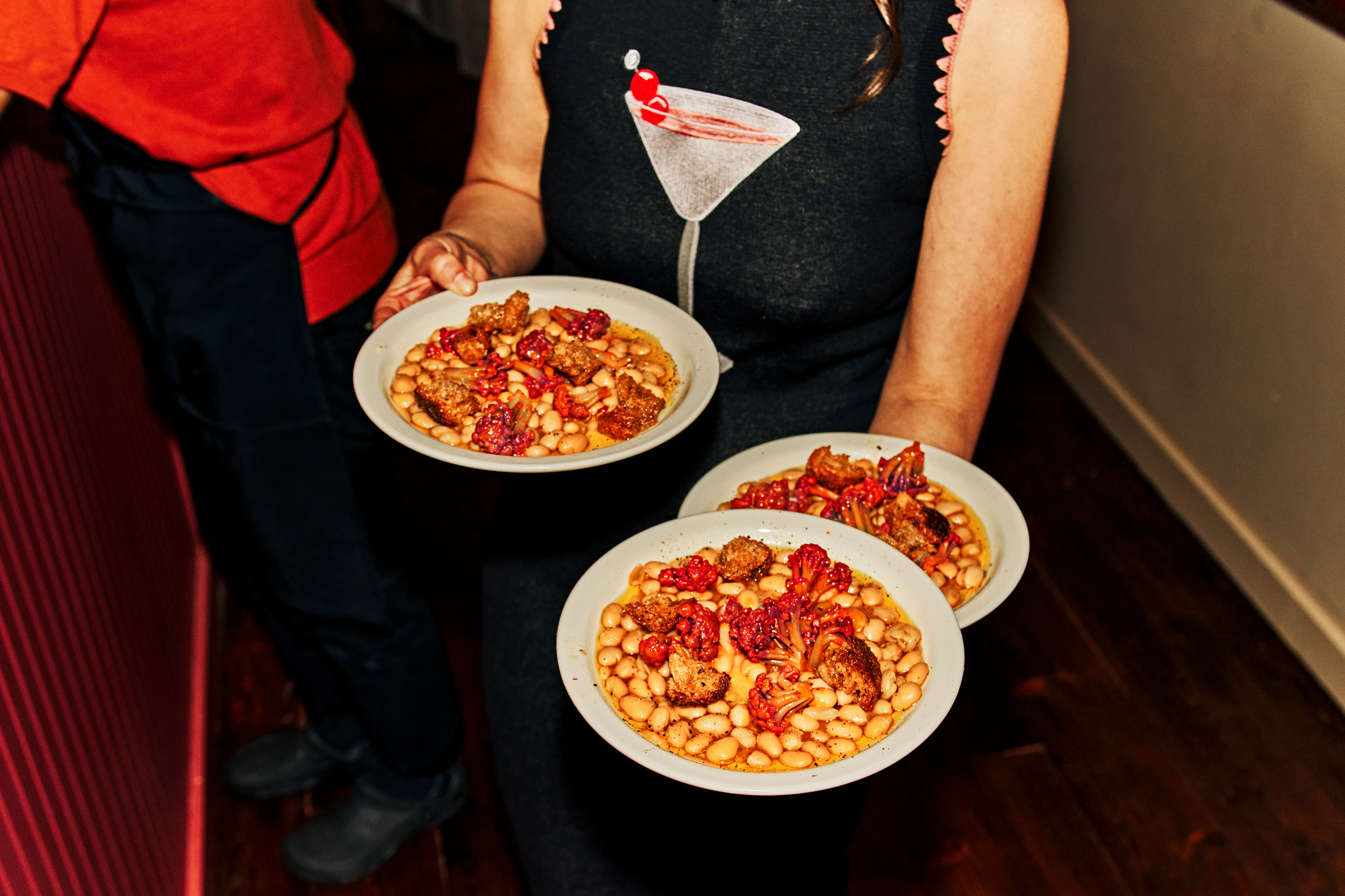 Someone holding up three plates of food with beans.
