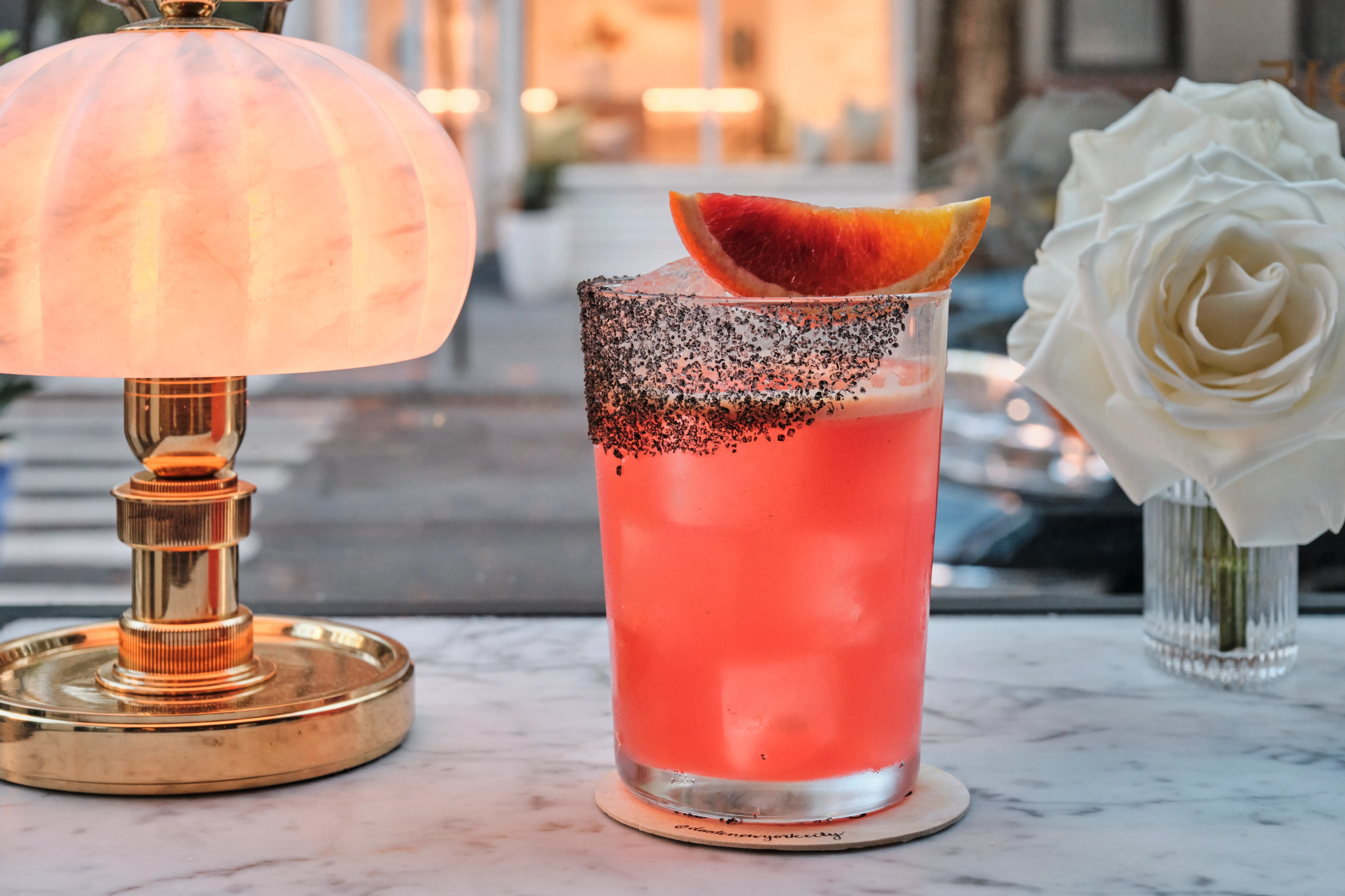 A pink-ish cocktaill with black salt on the glass and a fruit garnish.