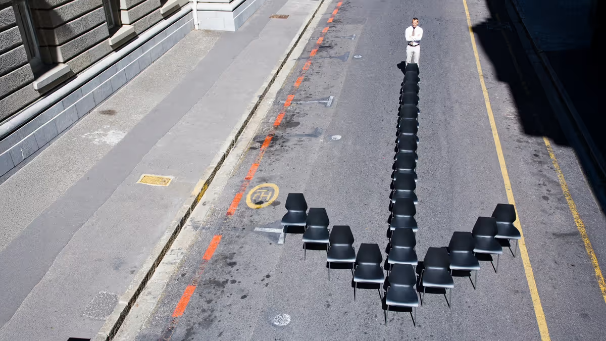 Photo of a person standing in the middle of a road with an arrow made of chairs.