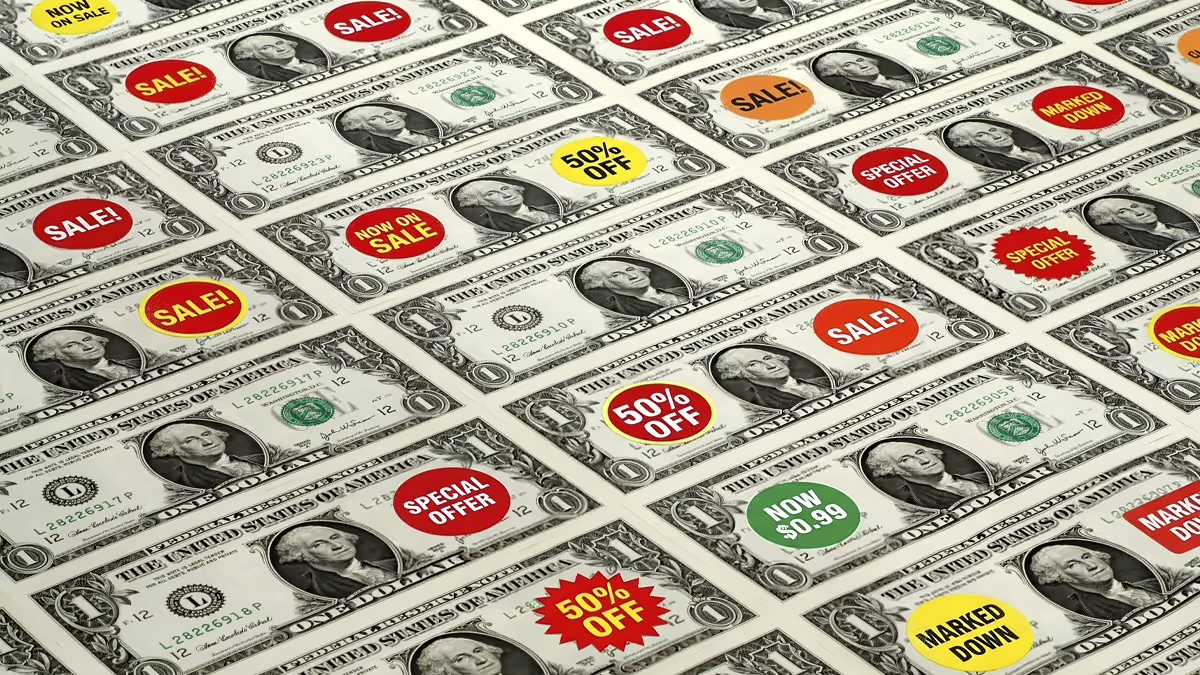 A grid of U.S. one-dollar bills, each overlaid with colorful retail-style stickers reading phrases like 'SALE!', '50% OFF', 'SPECIAL OFFER', and 'NOW $0.99', symbolizing consumerism and the commercialization of money.
