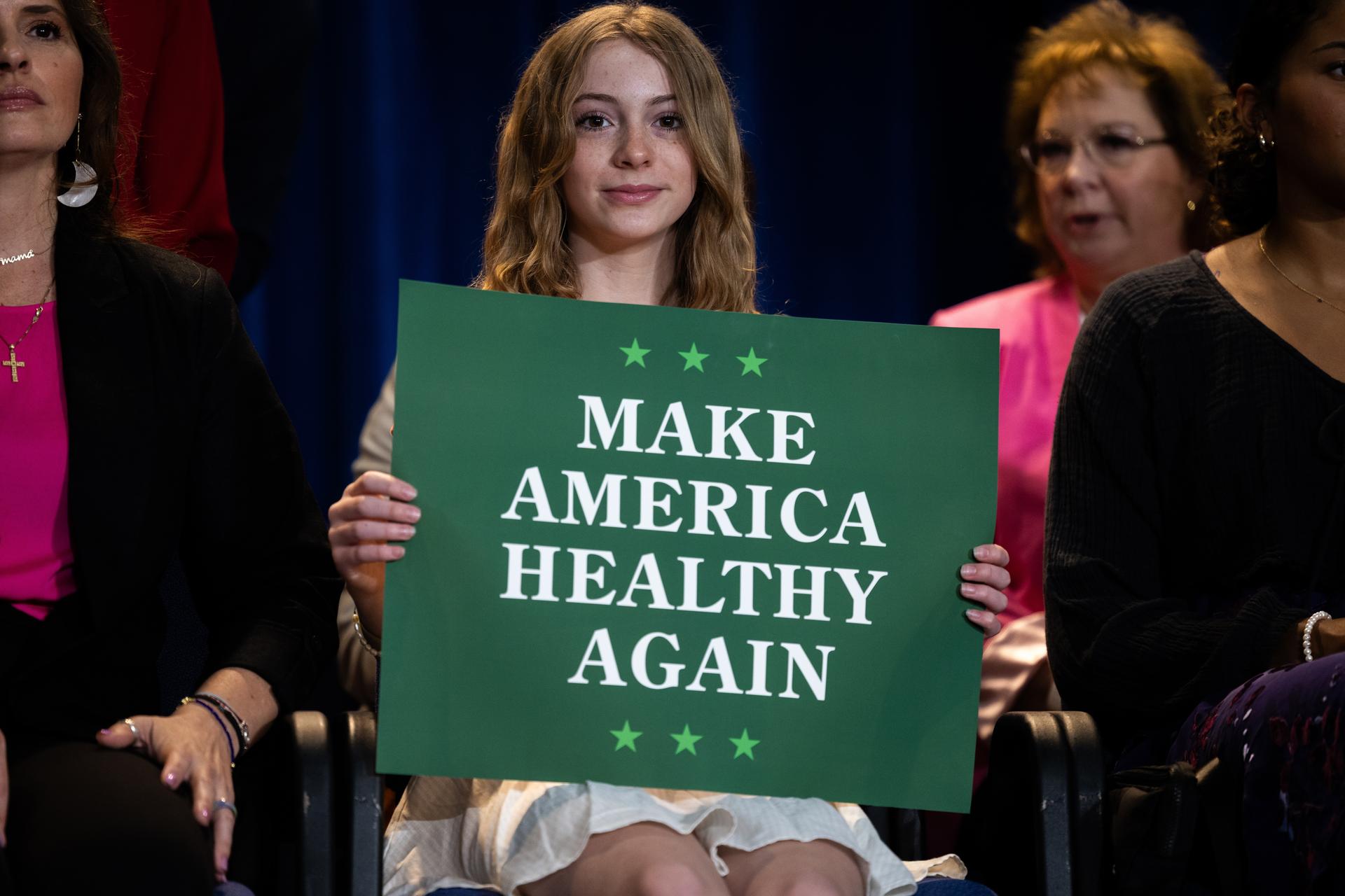 A young woman holds a green sign that says 
