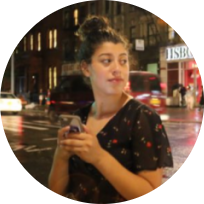 Izzie, a Latina woman with brown skin, wears her black hair in a bun; she wears a black dress with a cherry print.