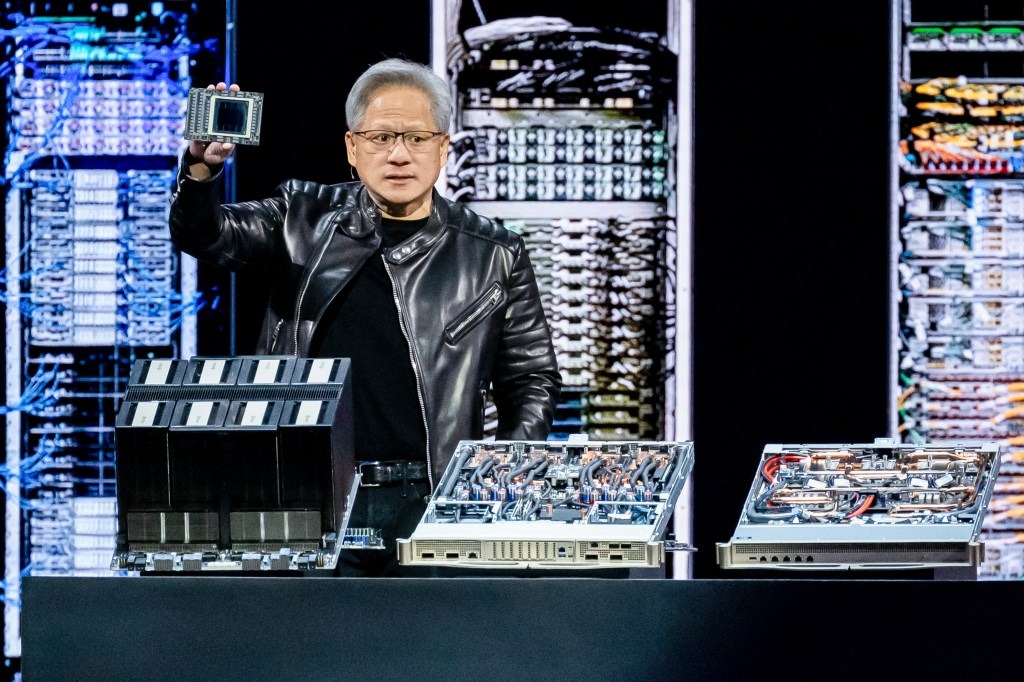 Jensen Huang, Nvidia CEO, in a black leather jacket, holding a computer chip.