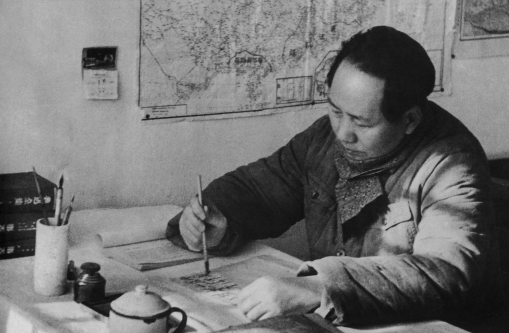 A black-and-white photo of a Chinese man writing at a desk.