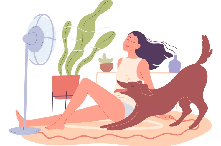 A woman sits in front of a fan with a dog by her side to escape summer heat.