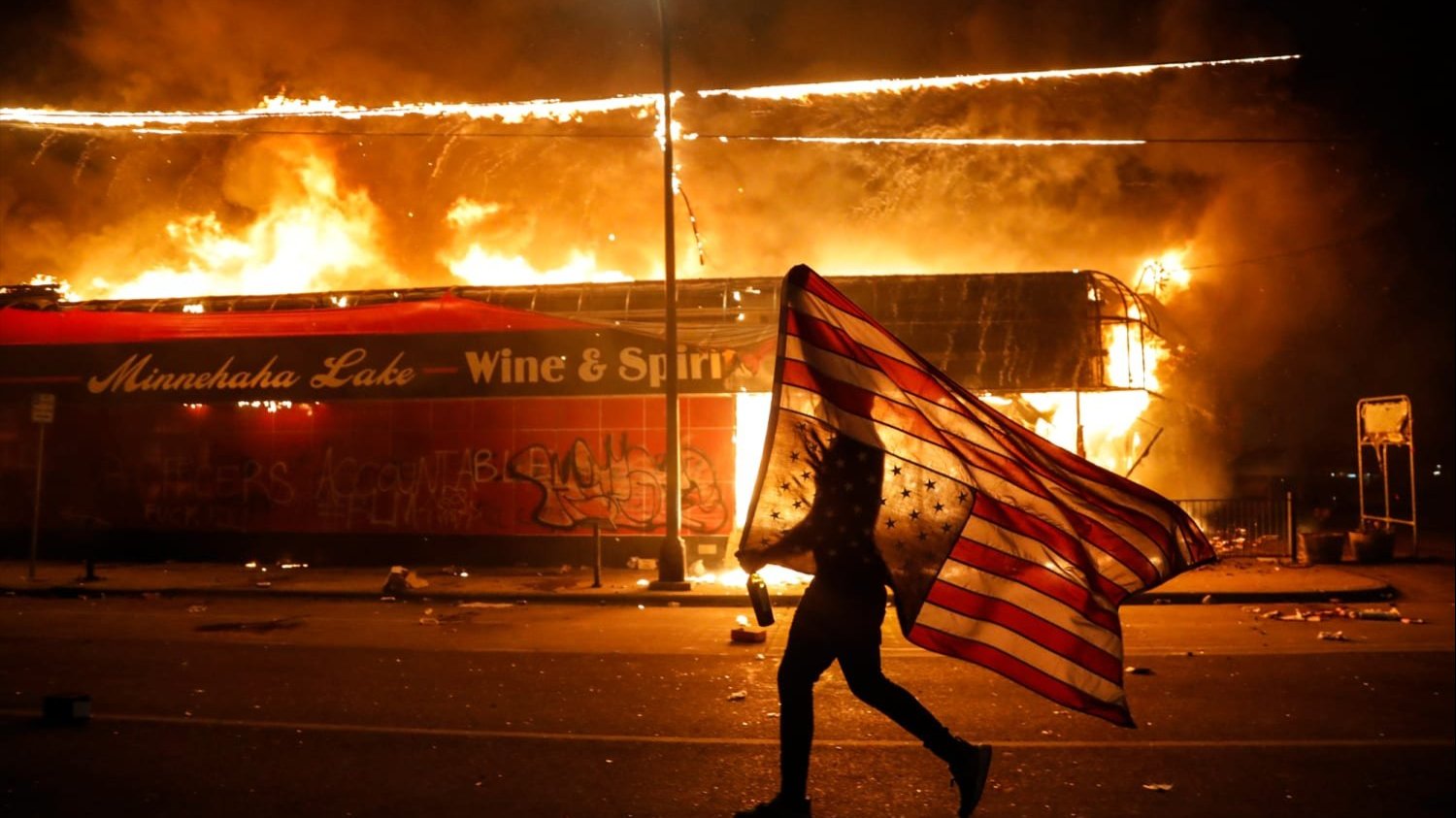 Person holding an American flag in front of a burning building