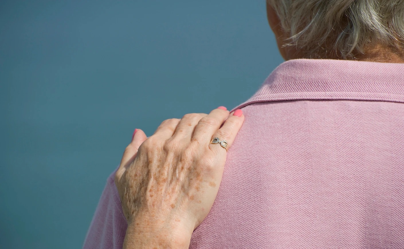 A comforting hand on the back of a woman wearing a pink sweater