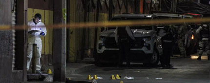 Forensic personnel work behind crime-scene tape in a street.