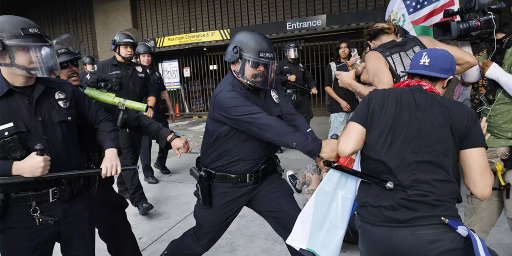 An LAPD officer in a riot helmet strikes a protester with a baton An LAPD officer in a riot helmet strikes a protester with a baton