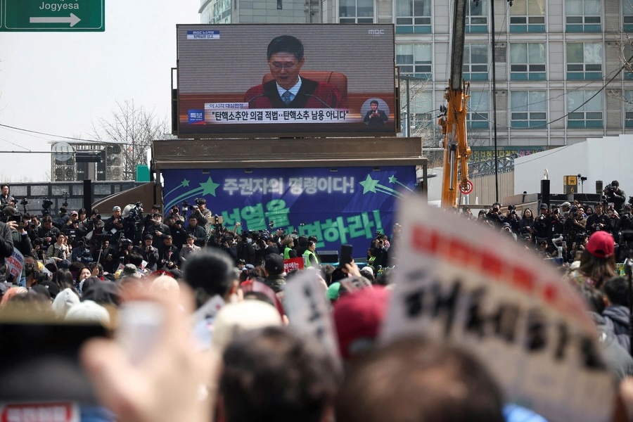 People watch a live news report as they wait for the Constitutional Court ruling on President Yoon Suk Yeol's impeachment, near the Constitutional Court in Seoul 