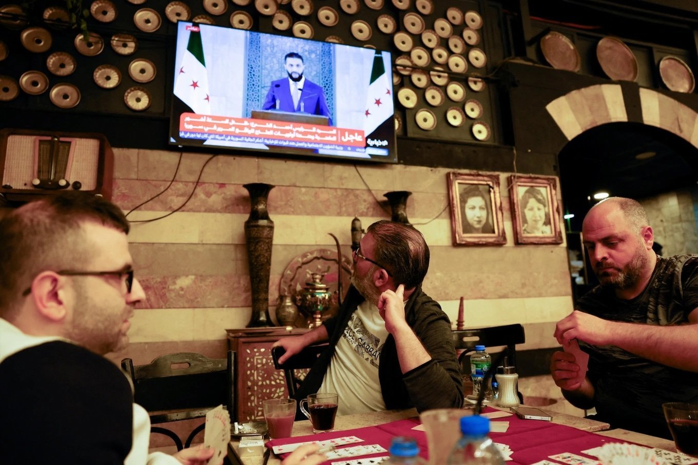 Men play cards at a coffee shop as Syrian President Ahmed al-Sharaa addresses the nation in a televised speech, in Damascus, Syria, on May 14.