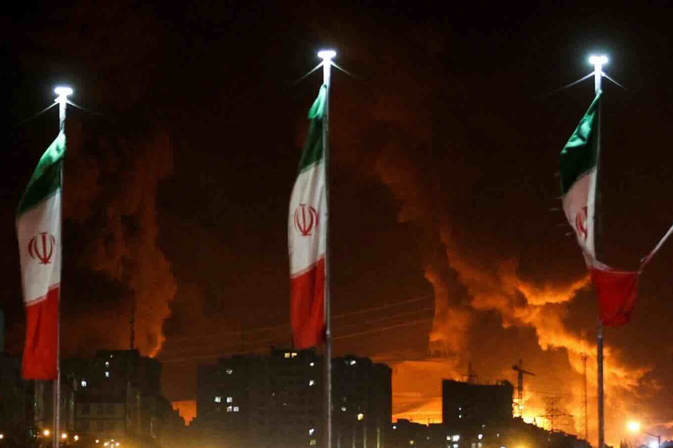 Iranian flags fly as fire and smoke from an Israeli attack on Sharan Oil depot rise, following Israeli strikes in Tehran on June 15, 2025.