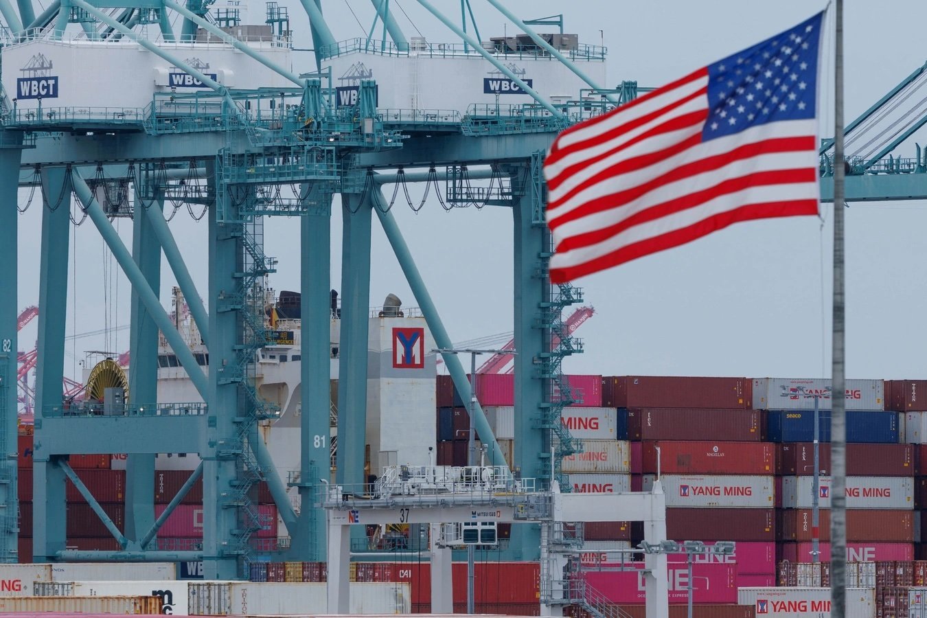 A U.S. flag flutters near shipping containers as a ship is unloaded at the Port of Los Angeles, in San Pedro, California, U.S., May 1, 2025.