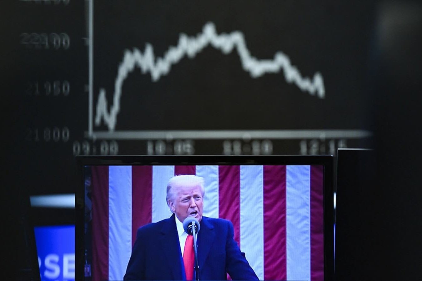 Behind a television monitor showing U.S. President Donald Trump, the display board with the Dax curve shows falling share prices on April 3, 2025 in Frankfurt, Germany. 