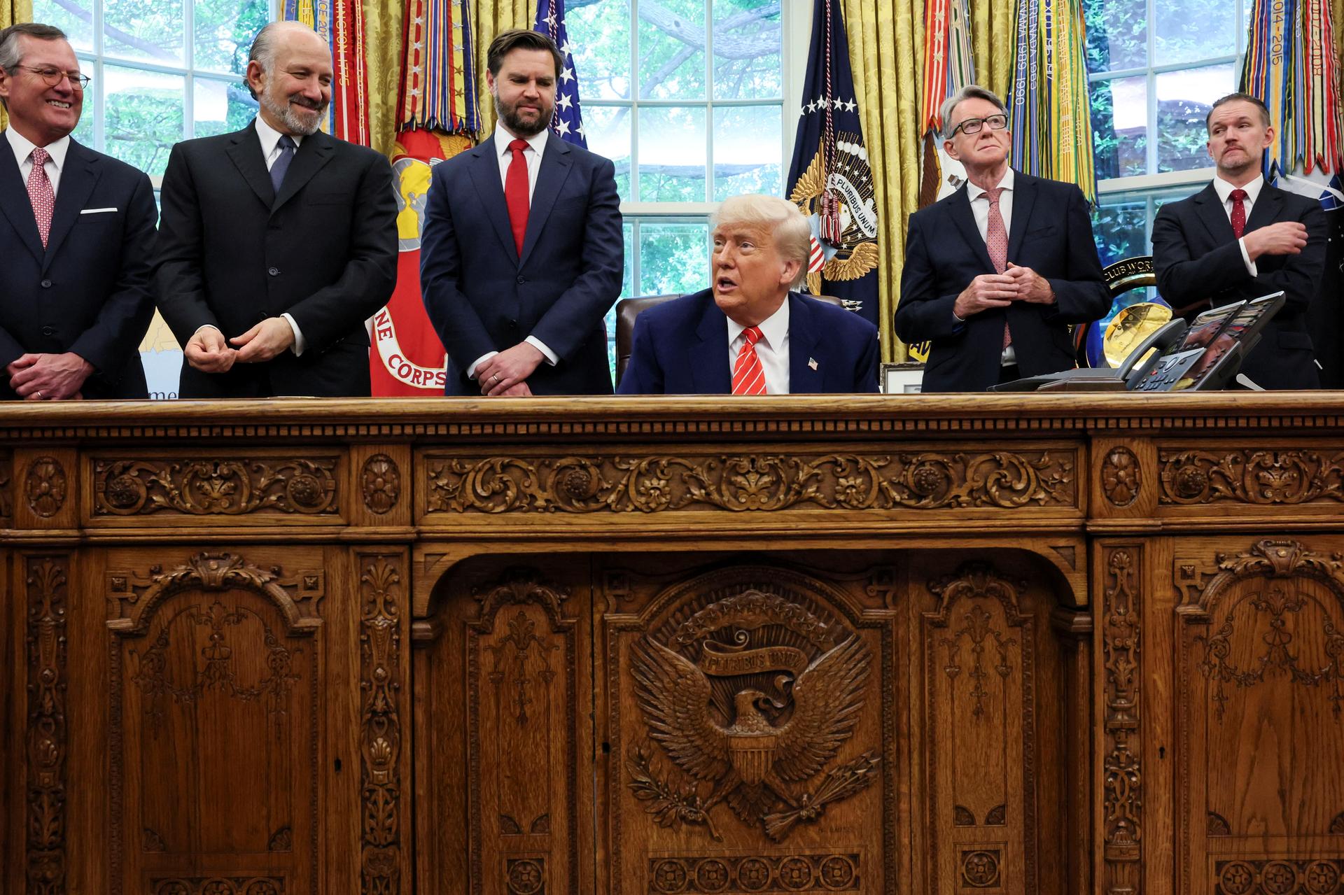 President Donald Trump is flanked by aides as he makes an announcement about a trade deal with the U.K., in the Oval Office at the White House in Washington, D.C., U.S., May 8, 2025.