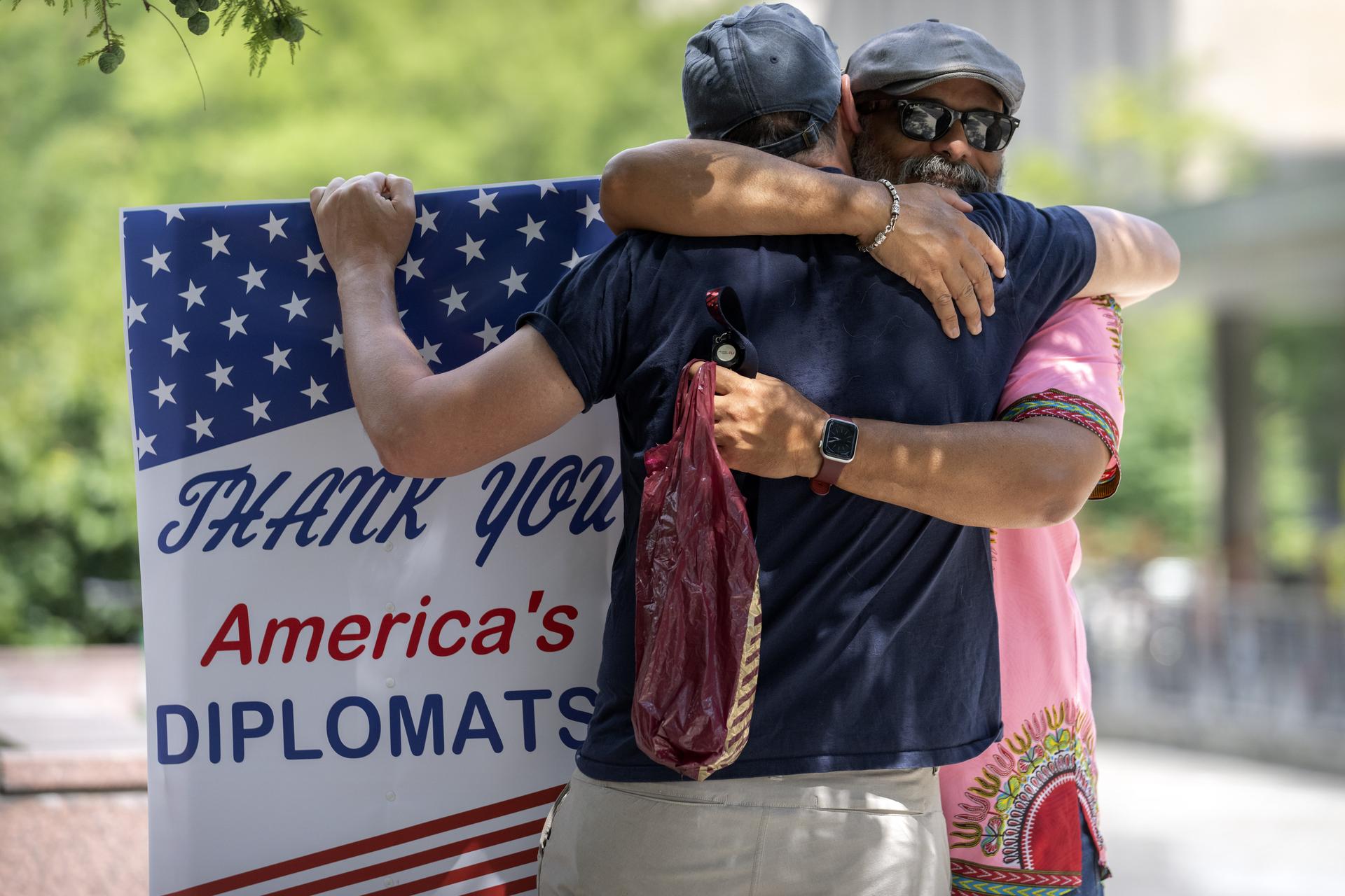 A man hugs former Foreign Service employee Bob Gilchrist, of Washington,, as he holds a sign reading Thank You America's Diplomats outside the State Department headquarters, July 11, in Washington. 