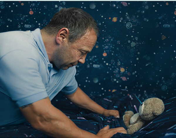An adult tucking a stuffed animal into a space themed bed.