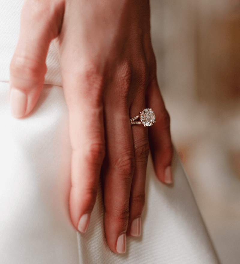 A hand rests against white fabric, showcasing a stunning engagement ring