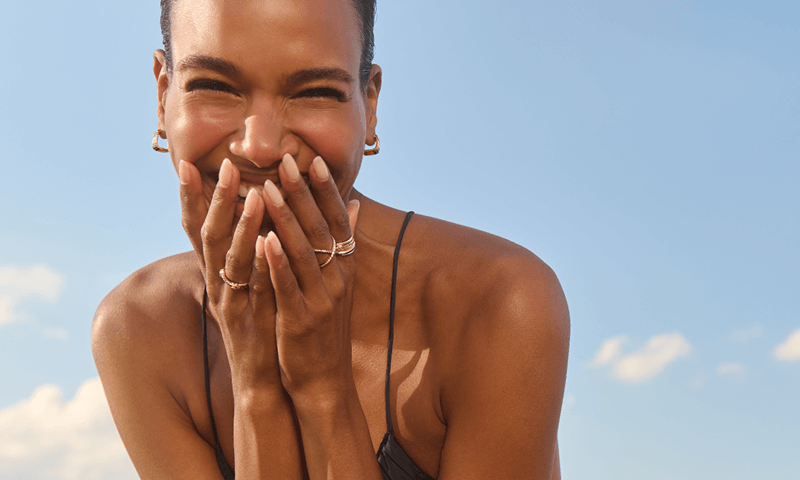 A woman laughs and holds her hands up to her face to reveal stunning rings and earrings