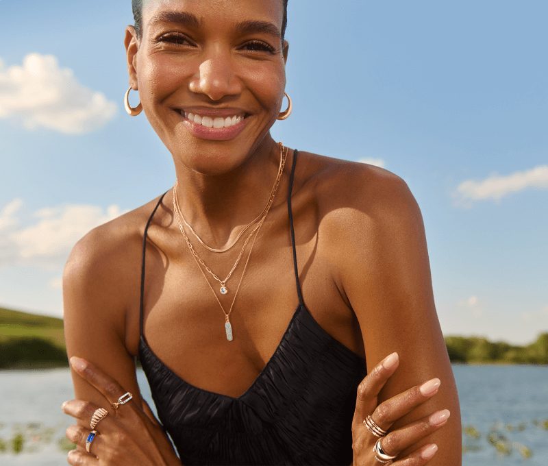 A woman wearing a black tank top showcases stunning earirngs, necklaces and rings