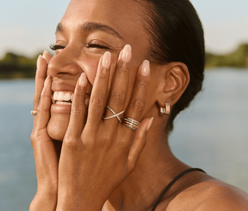 A woman holds her hands to her face, revealing stunning rings and earrings