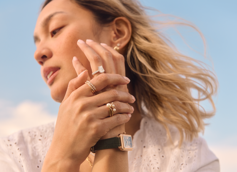 A woman showcases stunning jewelry — featuring delicate earrings, sparkling rings, and a luxurious watch.