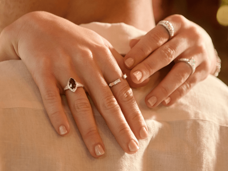 A woman's hands are draped over a pair of shoulders, revealing several stunning rings