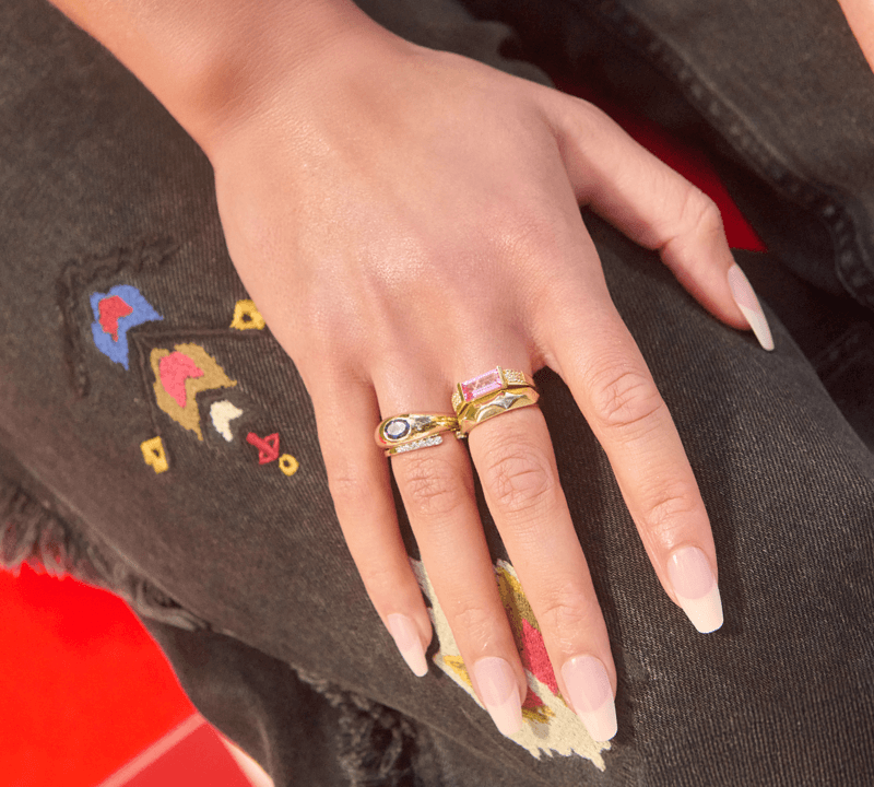 A woman's hand rests against her leg to reveal stacks of stunning rings on index and middle finger