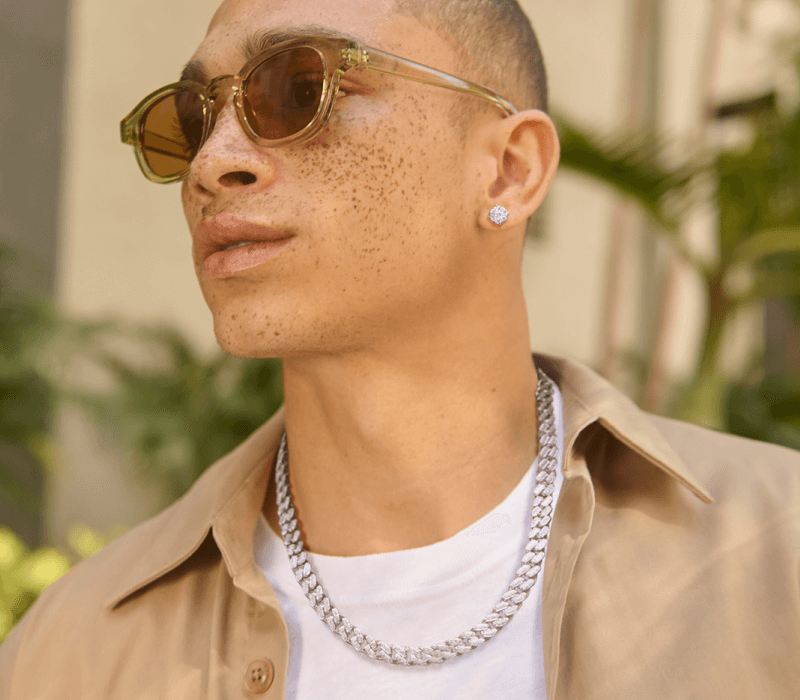 A man wearing sunglasses, chain necklace and stud earrings looks into the distance
