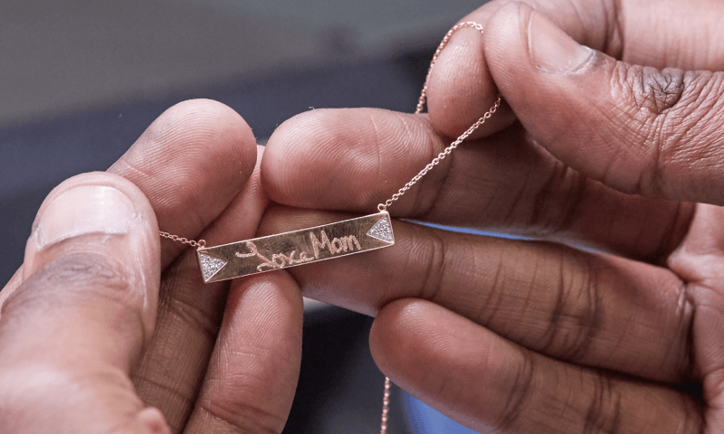 A pair of hands hold an engraved necklace