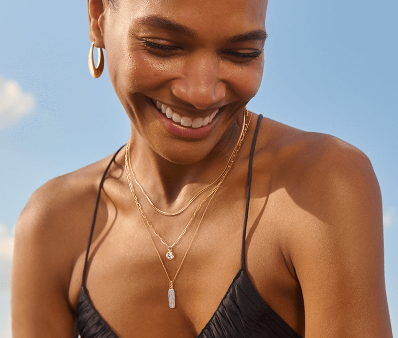 A woman gazes downward to reveal gold hoops and a stack of necklaces