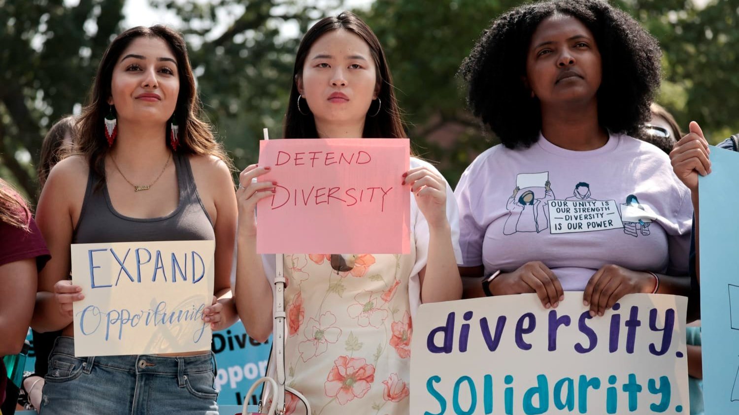 Three people hold signs that say ''expand opportunity,'' ''defend diversity'' and ''diversity, solidarity, equity.''