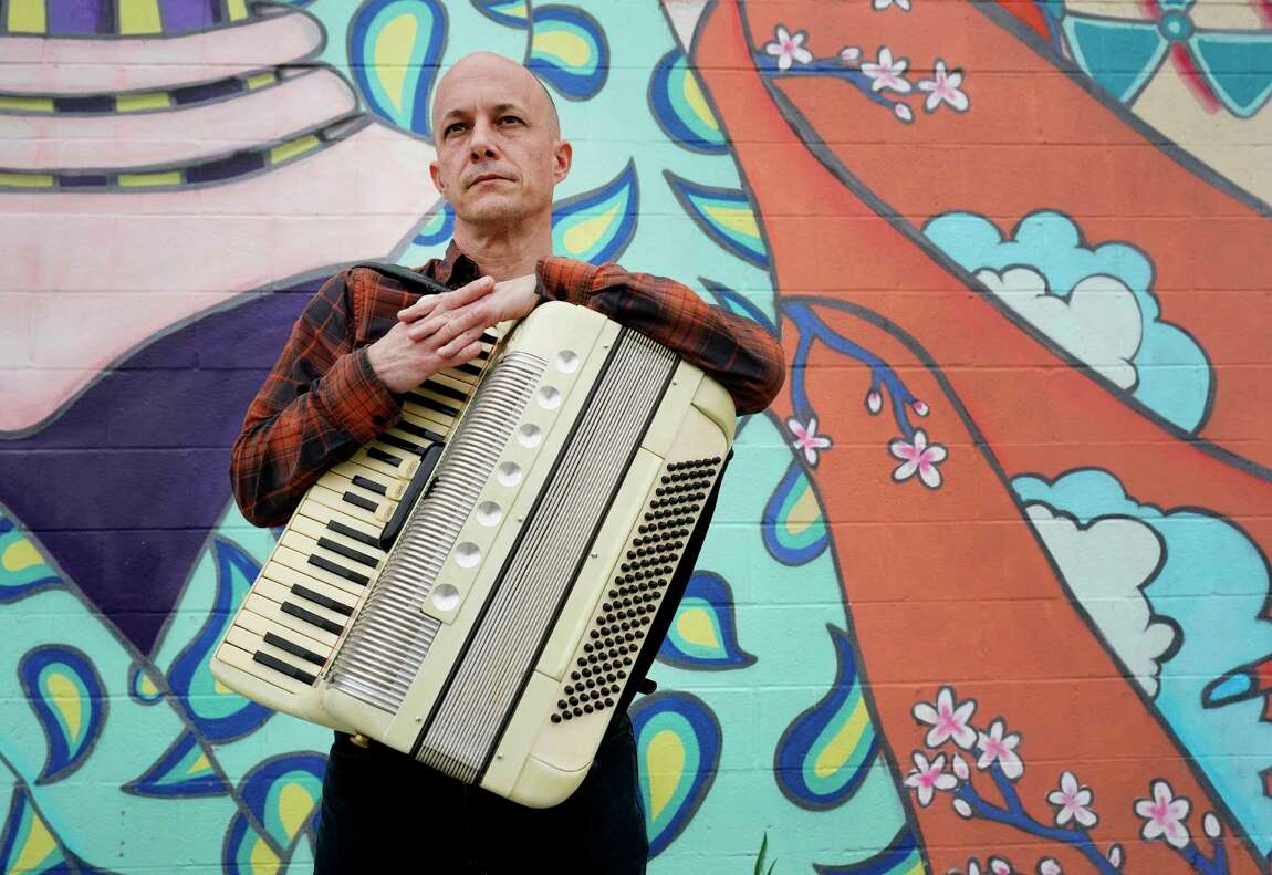 Anthony Barilla stands in front of a gratiffied wall holding an accordion.