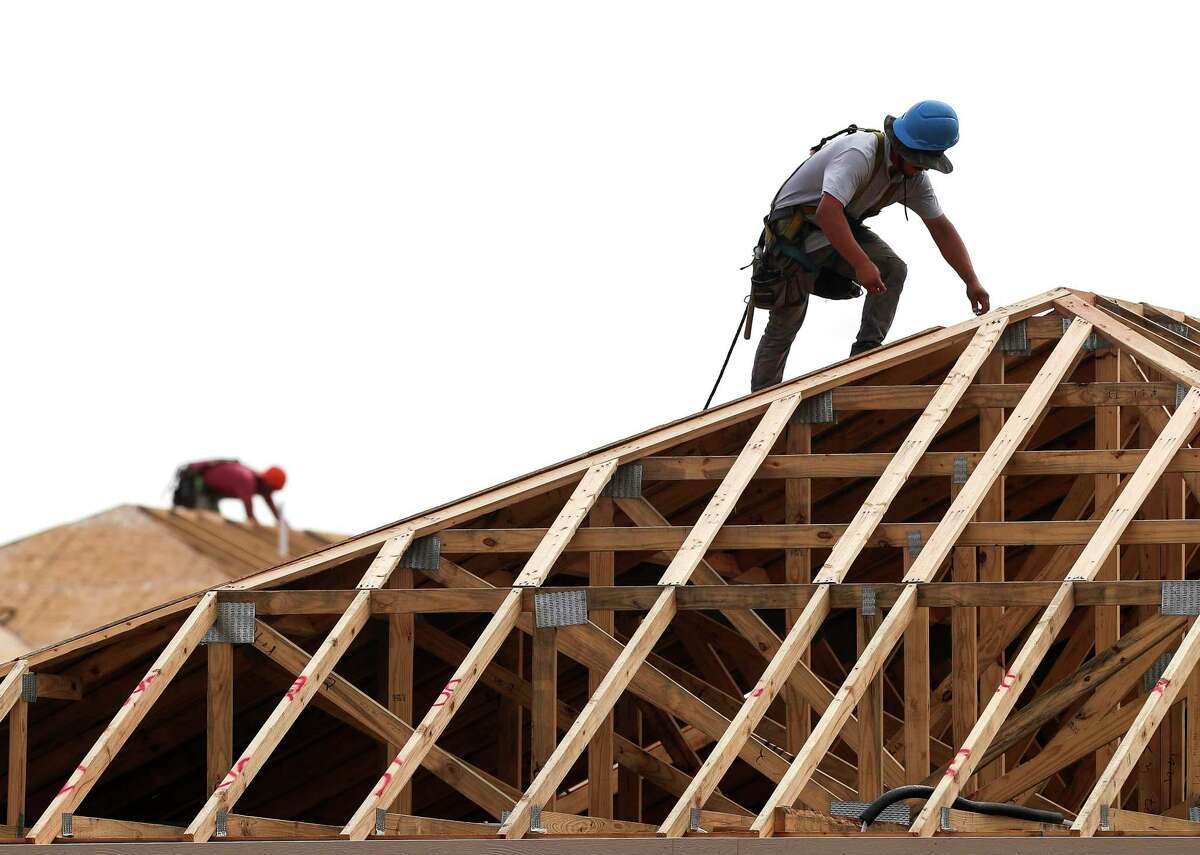 A man stands on the roof of a house working on its framing.