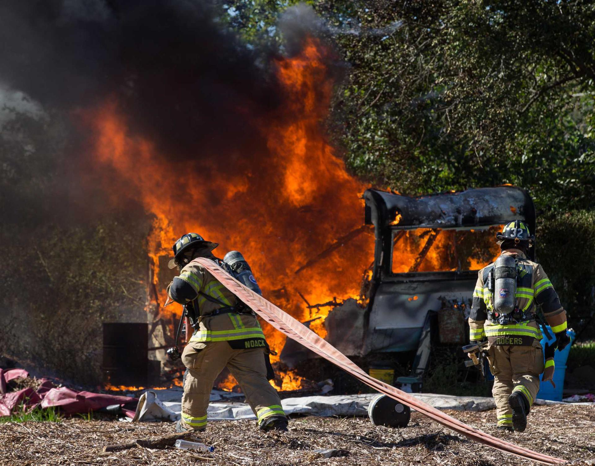 A fire fighter pulls a hose to fight the flames engulfing a bus.