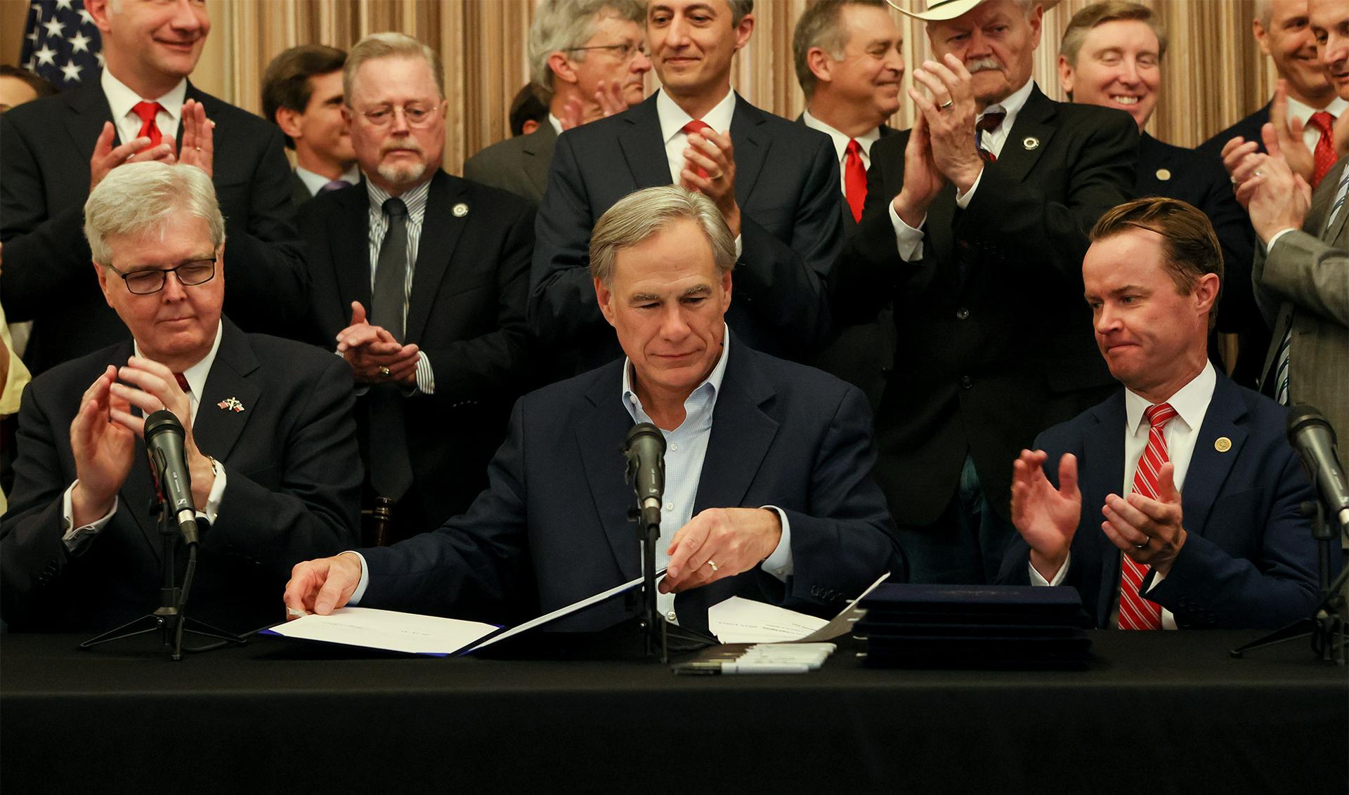 Texas Governor Greg Abbott, center, seated next to Lieutenant Governor Dan Patrick, left, and Speaker Dade Phelan prepares to sign a ''constitutional carry'' bill allowing Texans to carry handguns without a permit along with several other pieces of legislation.