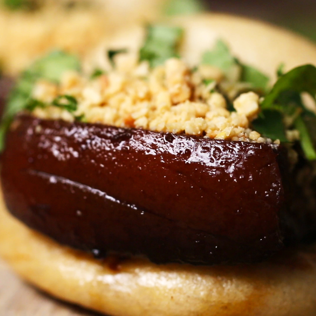 a close up of a thick slab of pork belly, glistening in the light, between fluffy buns and topped with crushed peanuts